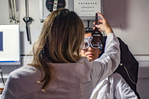 An optometrist performing an eye examination on a patient using a phoropter to test vision in a clinical setting.