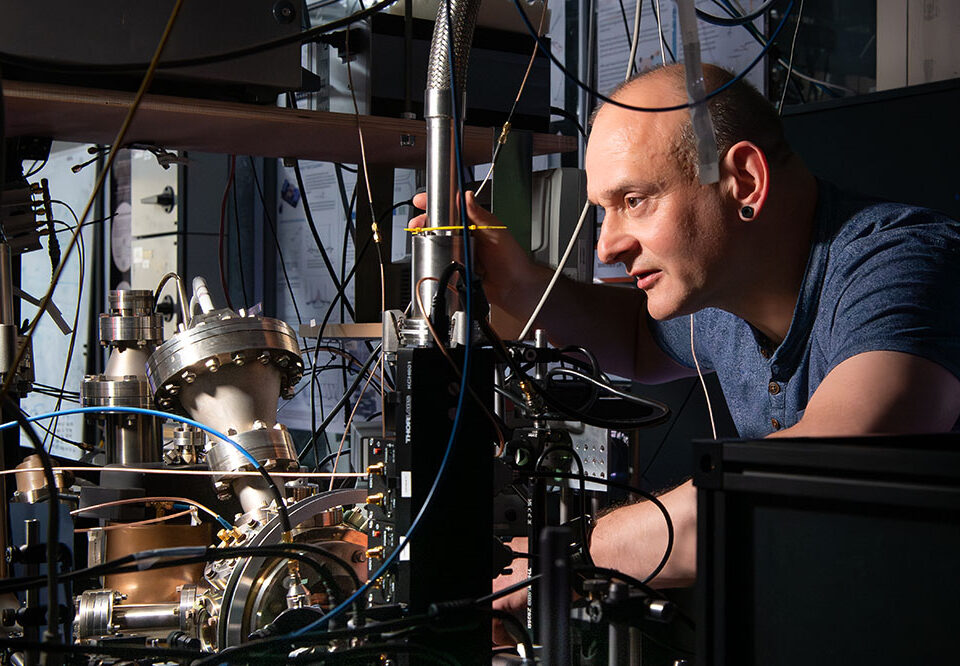 Researcher adjusting equipment in a laboratory surrounded by scientific instruments and cables.